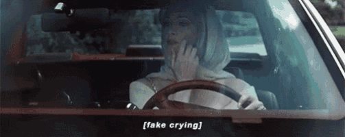 a woman is driving a car with the words `` fake crying '' on the windshield .