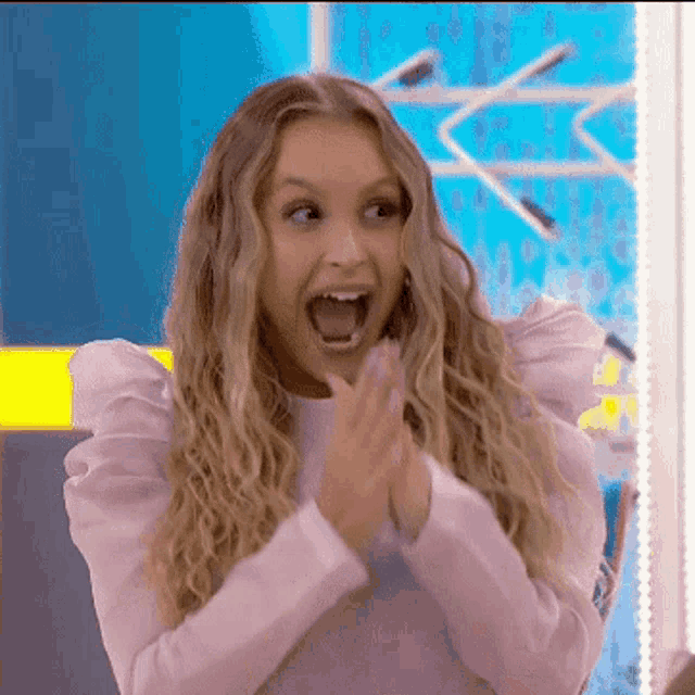 a woman with a surprised look on her face is clapping her hands .