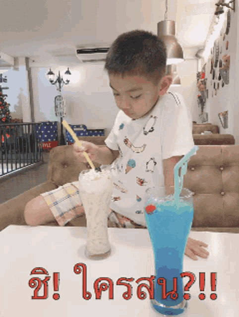 a young boy is sitting at a table with a milkshake and a blue drink with straws