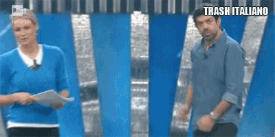 a man and a woman are standing next to each other in front of a blue wall with trash italiano written on it .