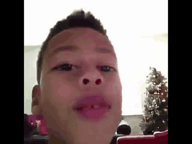 a young boy is making a funny face while sitting in front of a christmas tree .