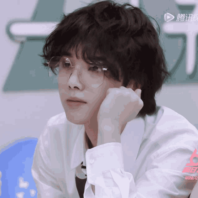 a close up of a person wearing glasses and a white shirt with chinese writing on the bottom right