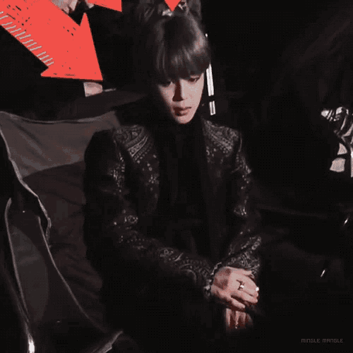 a man in a black jacket sits in a chair with a red arrow pointing to the right