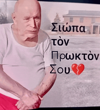 a man with a broken heart is standing in front of a screen with greek writing