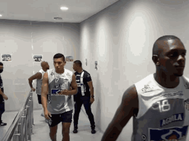a group of men are walking down a hallway and one has the number 18 on his shirt