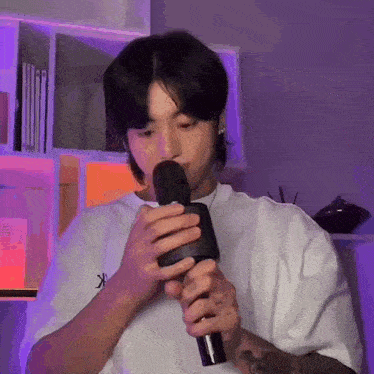 a young man is singing into a microphone while wearing a white shirt .