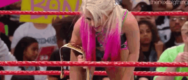 a woman with pink hair is kneeling in a wrestling ring holding a belt .