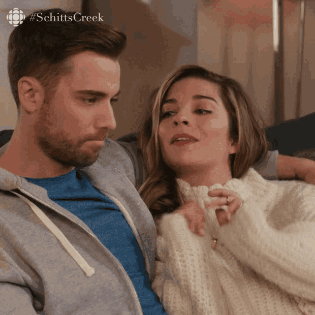 a man and a woman sitting on a couch with #schittscreek written on the bottom right