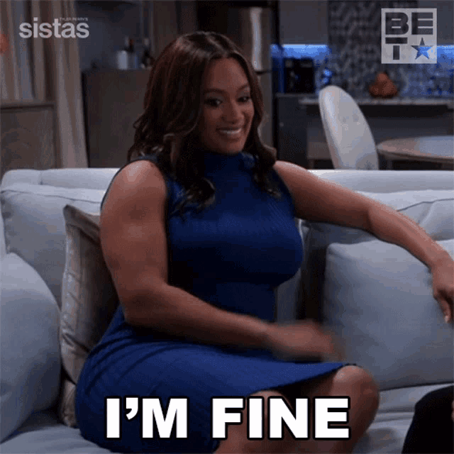 a woman in a blue dress is sitting on a couch and says " i 'm fine "
