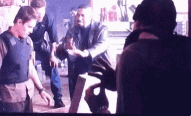a group of men are standing around a table and talking to each other in a room .