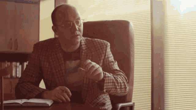 a man in a plaid jacket is sitting at a desk