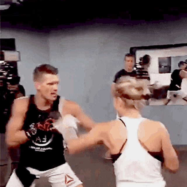 a man and a woman are boxing in a gym and the man is wearing a tank top that says reebok on it