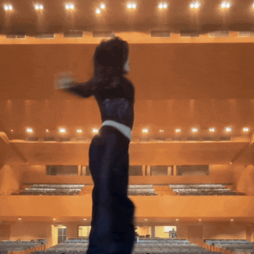 a woman in a black dress stands in a large auditorium