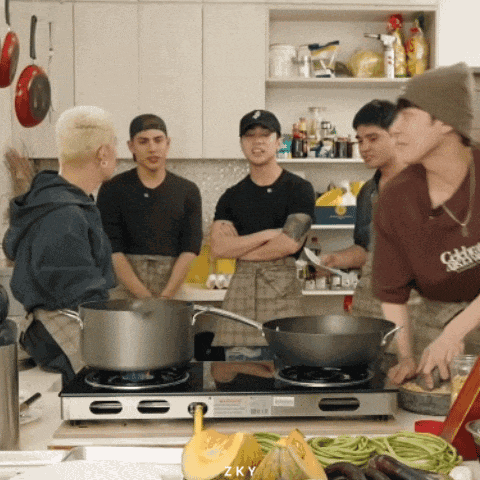 a group of young men are cooking in a kitchen and one of them is wearing a shirt that says okay