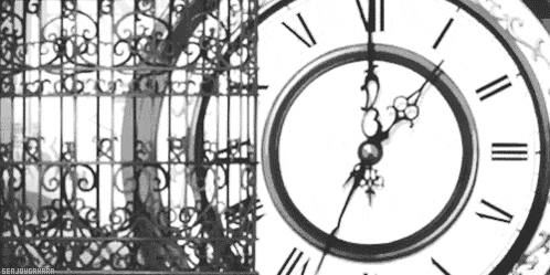 a black and white photo of a clock with roman numerals and a fence in the background .