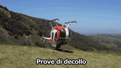 a red and white helicopter is sitting on top of a grassy hill with the words prove di decollo above it