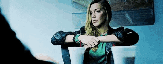 a woman is sitting at a table with her hands on her hips and looking at the camera .