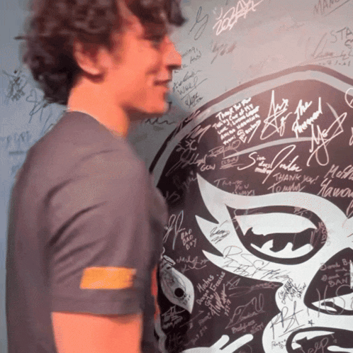 a man stands in front of a wall covered in signatures including one that says " thank you "