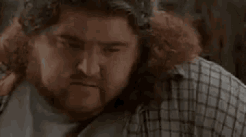 a man with a beard and curly hair is looking at the camera with the words `` what '' written in the background .