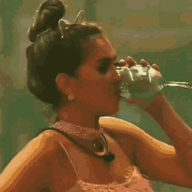a woman in a pink dress is drinking from a glass in a dark room .