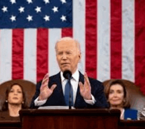a man in a suit and tie is standing at a podium in front of an american flag .