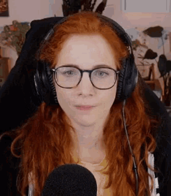 a woman with red hair and glasses is wearing headphones and sitting in front of a microphone .