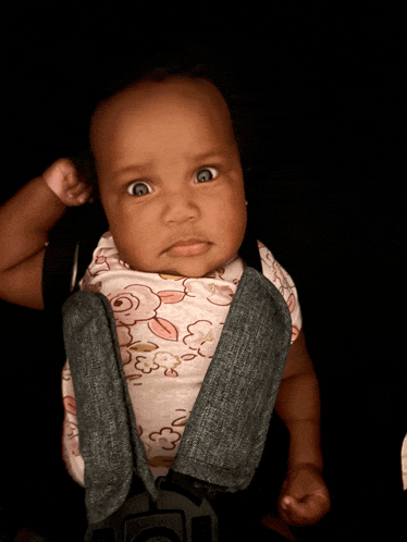 a baby wearing a floral shirt and jeans is sitting in a car seat