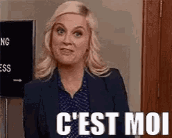 a woman in a suit is standing in front of a sign that says `` c ' est moi '' .