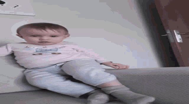 a baby is sitting on a couch wearing socks and a pink shirt with a train on it .