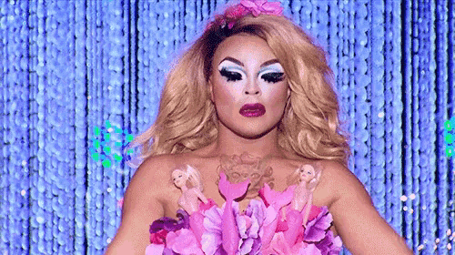 a drag queen is holding a bouquet of pink flowers on her body .