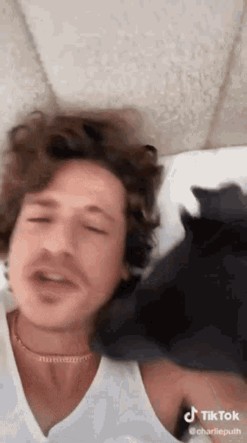a man is laying on a bed with a black cat on his shoulder .