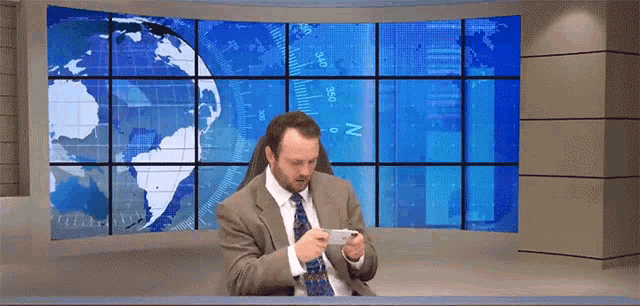 a man in a suit and tie is looking at his phone in front of a large screen that says n on it