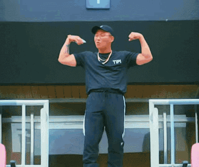 a man wearing a black shirt with the word tipi on it flexes his muscles