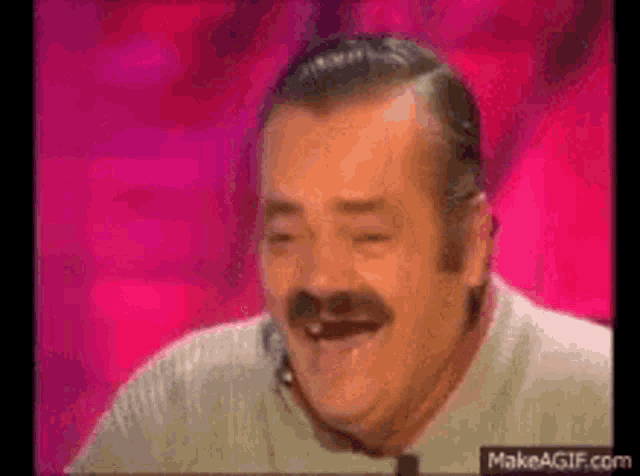 a man with a mustache is laughing while sitting on a stage .