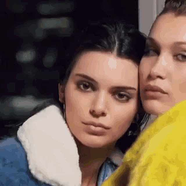 two women are standing next to each other and looking at the camera . one of the women is wearing a denim jacket .