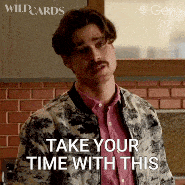a man with a mustache is standing in front of a brick wall and says " take your time with this "