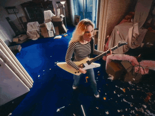 a woman in a striped shirt is holding a guitar in a messy room