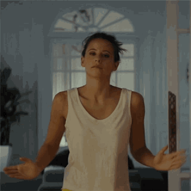 a woman in a white tank top has her hair in a messy bun