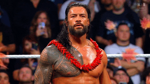 roman reigns is wearing a lei and standing in a wrestling ring in front of a crowd .