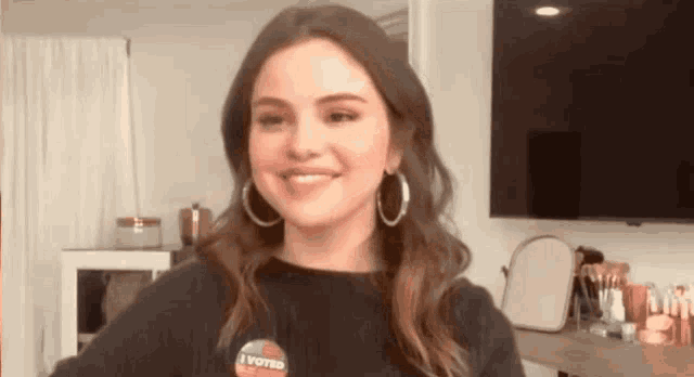 a woman wearing a black shirt and hoop earrings is smiling in a room .
