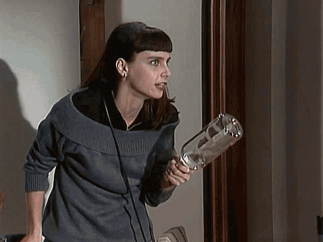 a woman in a gray sweater is holding a glass bottle in her hand .