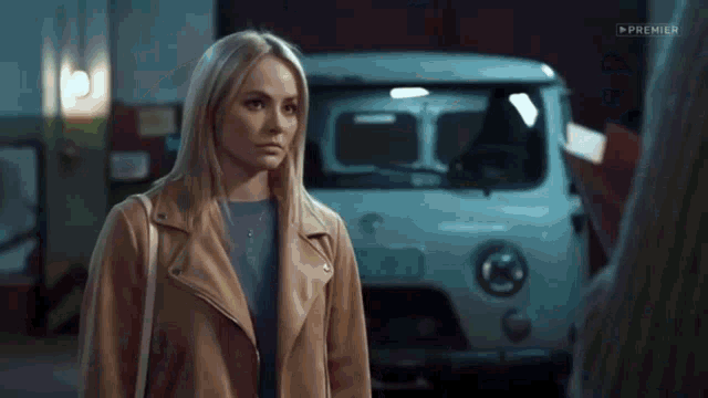 a woman in a tan jacket is standing in front of a white van .