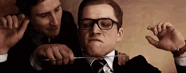 two men in suits are cutting a man 's neck with a knife .