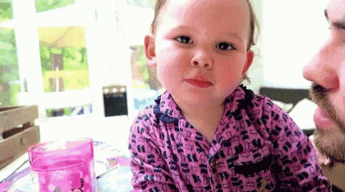 a little girl in a pink shirt is sitting next to a man with a beard .