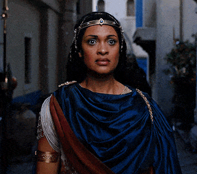 a woman wearing a blue robe and a gold headband looks at the camera