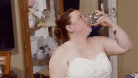 a woman in a wedding dress is drinking from a glass of wine .