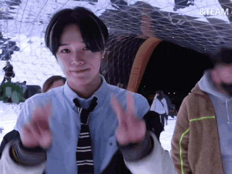 a young man wearing a tie and a blue shirt is giving the peace sign .