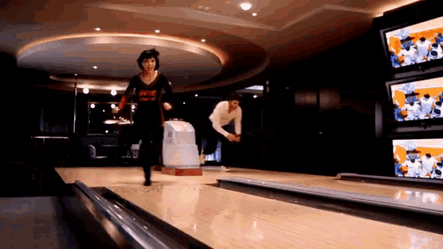 a man and a woman are bowling on a bowling alley in front of televisions