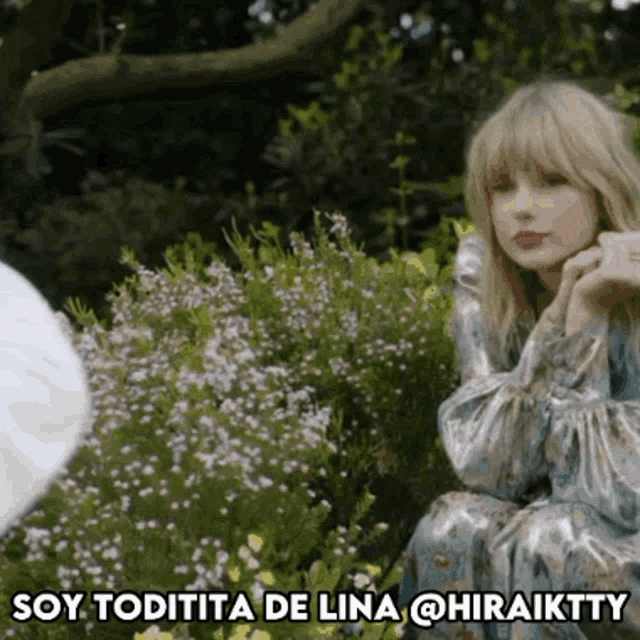 a woman is sitting in front of a bush with purple flowers and says soy toditita de lina @hiraiktty