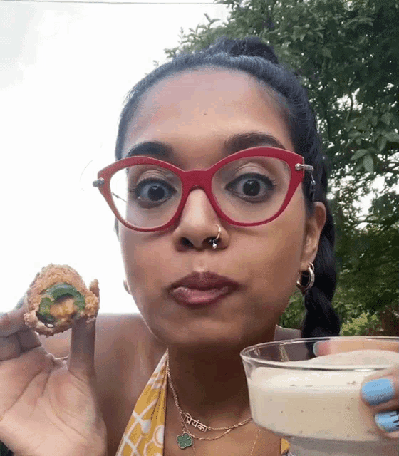 a woman wearing red glasses is holding a glass of milk and a fried food item